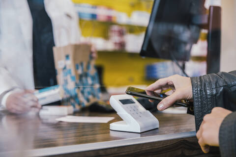Hand of customer with mobile phone at checkout counter in chemist shop stock photo