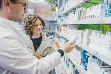 Apotheker, der einer lächelnden Kundin in einer Apotheke ein Medikament empfiehlt - MFF06844