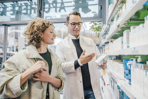 Apotheker, der einer lächelnden Kundin in einer Apotheke ein Medikament empfiehlt - MFF06845