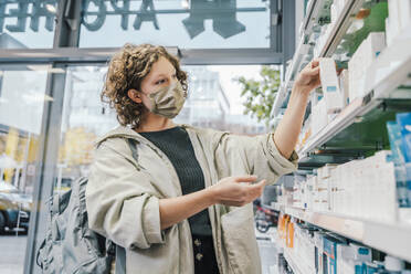 Female customer wearing protective face mask while checking medicine in chemist shop - MFF06849