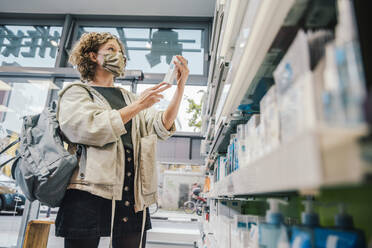 Female customer wearing protective face mask while checking medicine in chemist store - MFF06850