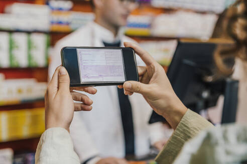 Hand eines Kunden, der sein Smartphone für ein Rezept in einer Apotheke benutzt - MFF06854