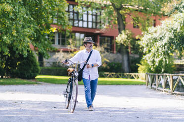 Älterer Mann mit Fahrrad auf dem Fußweg in einem öffentlichen Park - DGOF01643