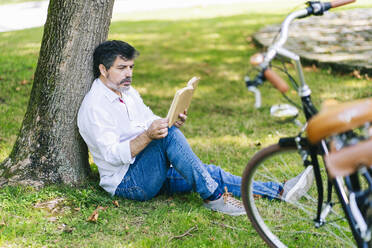 Älterer Mann liest konzentriert ein Buch, während er in einem öffentlichen Park sitzt - DGOF01652