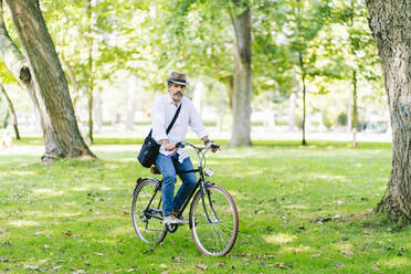 Älterer Mann mit Hut auf dem Fahrrad im Park - DGOF01667