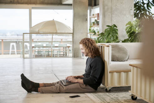 Mittlerer erwachsener Mann mit Laptop auf dem Boden sitzend zu Hause - FMKF06674