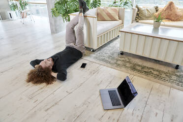 Langhaariger Mann auf dem Boden liegend im Wohnzimmer zu Hause - FMKF06676