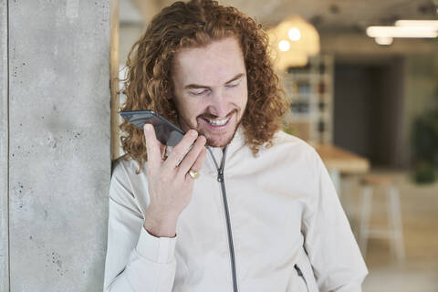 Man smiling while listening audio through smart phone leaning on column at home stock photo