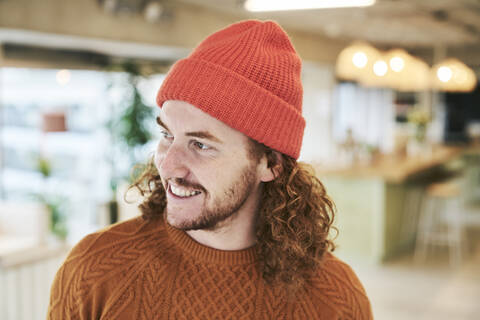 Lächelnder Hipster-Mann mit roter Strickmütze zu Hause, lizenzfreies Stockfoto