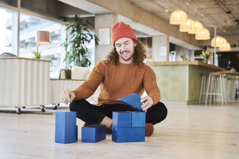 Mid adult man playing with toy block while sitting on floor in living room at home - FMKF06722