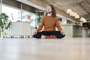 Hipster Mann mit gekreuzten Beinen sitzen auf dem Boden im Wohnzimmer zu Hause - FMKF06724