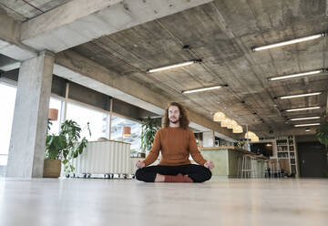 Man meditating while sitting on floor in living room at home - FMKF06725