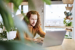 Mittlerer Erwachsener, der einen Laptop benutzt, während er zu Hause sitzt - FMKF06729