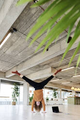 Hipster man doing hand stand in living room at home - FMKF06749