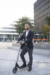 Male business person with electric scooter against building in city - HMEF01156