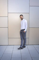 Confident entrepreneur with hands in pockets standing against wall - HMEF01167