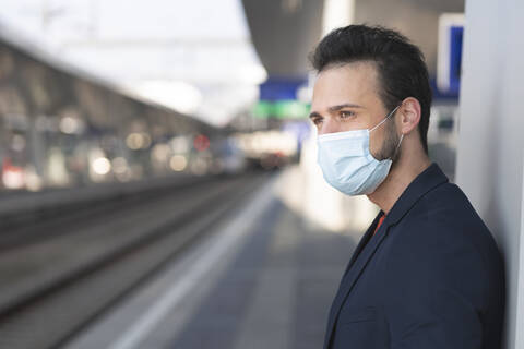 Male entrepreneur looking away while wearing protective mask on railroad station platform stock photo