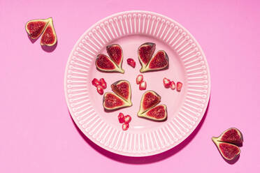 Directly above shot of fig slices arranged in plate over pink background - GEMF04388