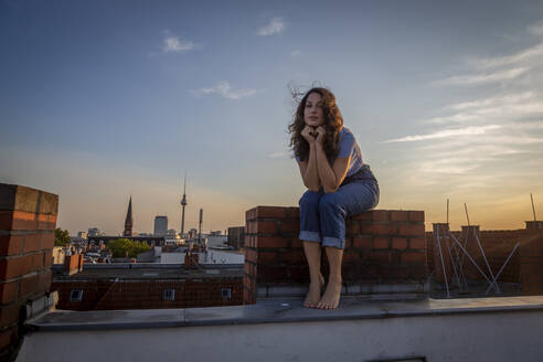 Contemplating woman sitting on rooftop against sky during sunset - NGF00711