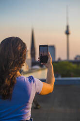 Frau, die auf dem Dach stehend mit ihrem Smartphone fotografiert - NGF00712