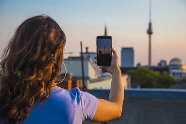 Frau beim Fotografieren mit dem Smartphone auf dem Dach während des Sonnenuntergangs - NGF00713