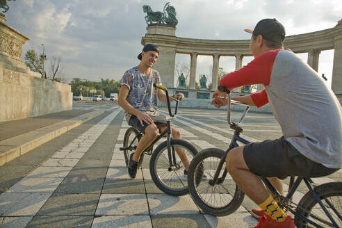 Junge männliche BMX-Fahrer, die auf Fahrrädern sitzend auf dem Heldenplatz eine Pause machen, Budapest, Ungarn - AJOF00548