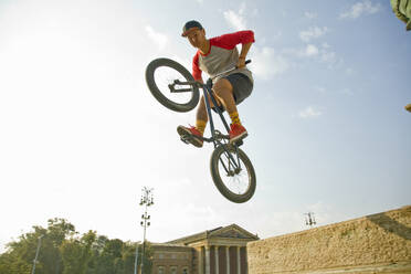 Young Asian man doing mid-air stunt on BMX bike against sky, Hero's Square, Budapest, Hungary - AJOF00550