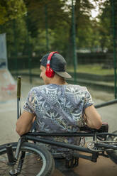 Junger Mann hört Musik, während er sich auf einem BMX-Fahrrad in einem Skateboard-Park entspannt - AJOF00561