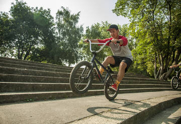 Junger asiatischer Mann macht Wheelie-Stunt mit BMX-Fahrrad auf Stufen im öffentlichen Park - AJOF00562