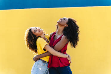 Junge Freundinnen umarmen sich an einer gelben Wand - RDGF00217