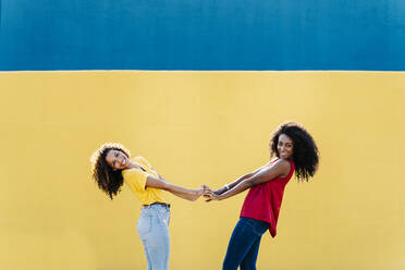 Smiling young lesbian couple holding hands against blue and yellow wall - RDGF00218