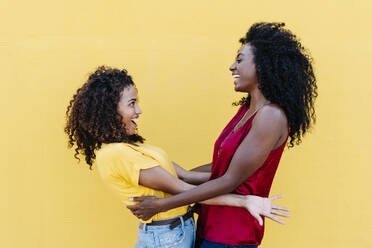 Lesbisches Paar, das sich lachend an einer gelben Wand betrachtet - RDGF00222