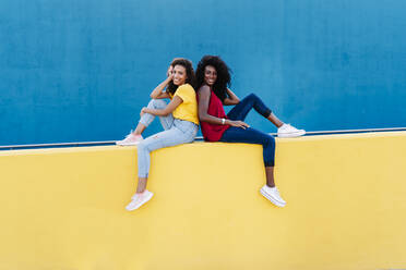 Happy couple sitting back to back on yellow retaining wall - RDGF00227