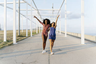 Happy young female friends walking with arms raised - RDGF00237