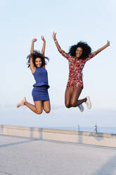 Cheerful female friends jumping at rooftop of building - RDGF00248