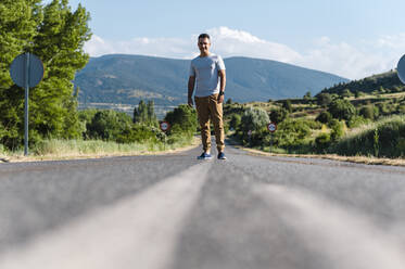 Young man standing in middle of road on sunny day - JMPF00583