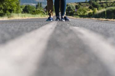 Young couple standing in middle of road on sunny road - JMPF00585