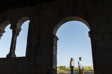 Junges Paar auf einem Feld stehend durch einen Bogen in einer römischen Kirche gesehen - JMPF00593