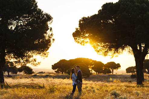 Romantic young couple standing on agricultural field against clear sky during sunset - JMPF00598