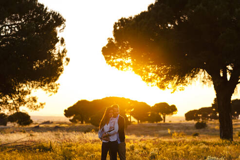 Romantisches junges Paar steht auf einem landwirtschaftlichen Feld bei Sonnenuntergang - JMPF00599