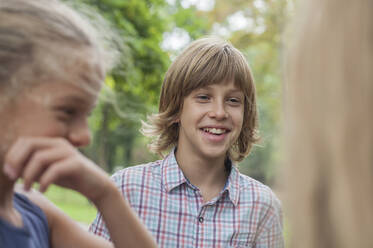 Happy boy talking with friends while standing in public park - AJOF00568