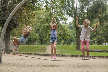 Glücklicher Junge und Mädchen hängen an einem Seil auf einem Spielplatz im Park - AJOF00571