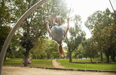 Girl doing back flip while holding ropes of outdoor play equipment in park - AJOF00572