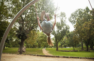 Mädchen, das einen Rückwärtssalto macht, während es Seile von Outdoor-Spielgeräten im Park hält - AJOF00572
