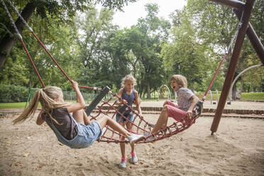 Boy and girls having fun while playing on rope swing at playground - AJOF00573