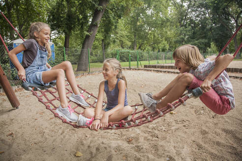 Fröhlicher Junge und Mädchen spielen auf einer Seilschaukel auf einem Spielplatz - AJOF00574