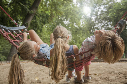 Children relaxing on rope swing in park - AJOF00575