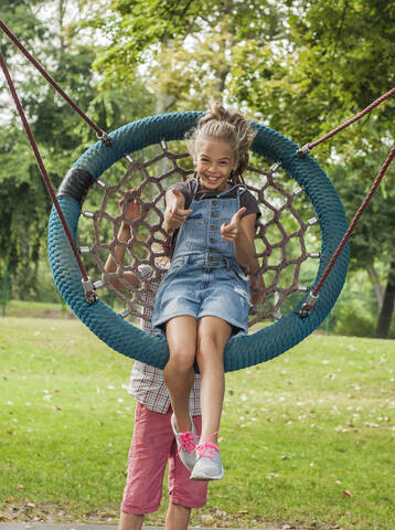Junge schiebt fröhliches Mädchen, das auf einer Seilschaukel im Park sitzt, lizenzfreies Stockfoto