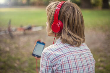 Junge hört Musik aus Kopfhörern in einem öffentlichen Park - AJOF00594