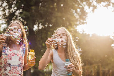 Girls blowing bubbles in park during sunset - AJOF00597